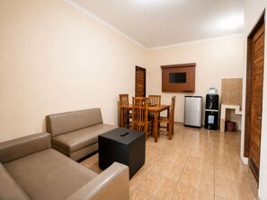 A compact living space with a sofa, a dining table with chairs, a small refrigerator, and a television mounted on the wall. - New Dgyp Resort Ciater (Ciater)