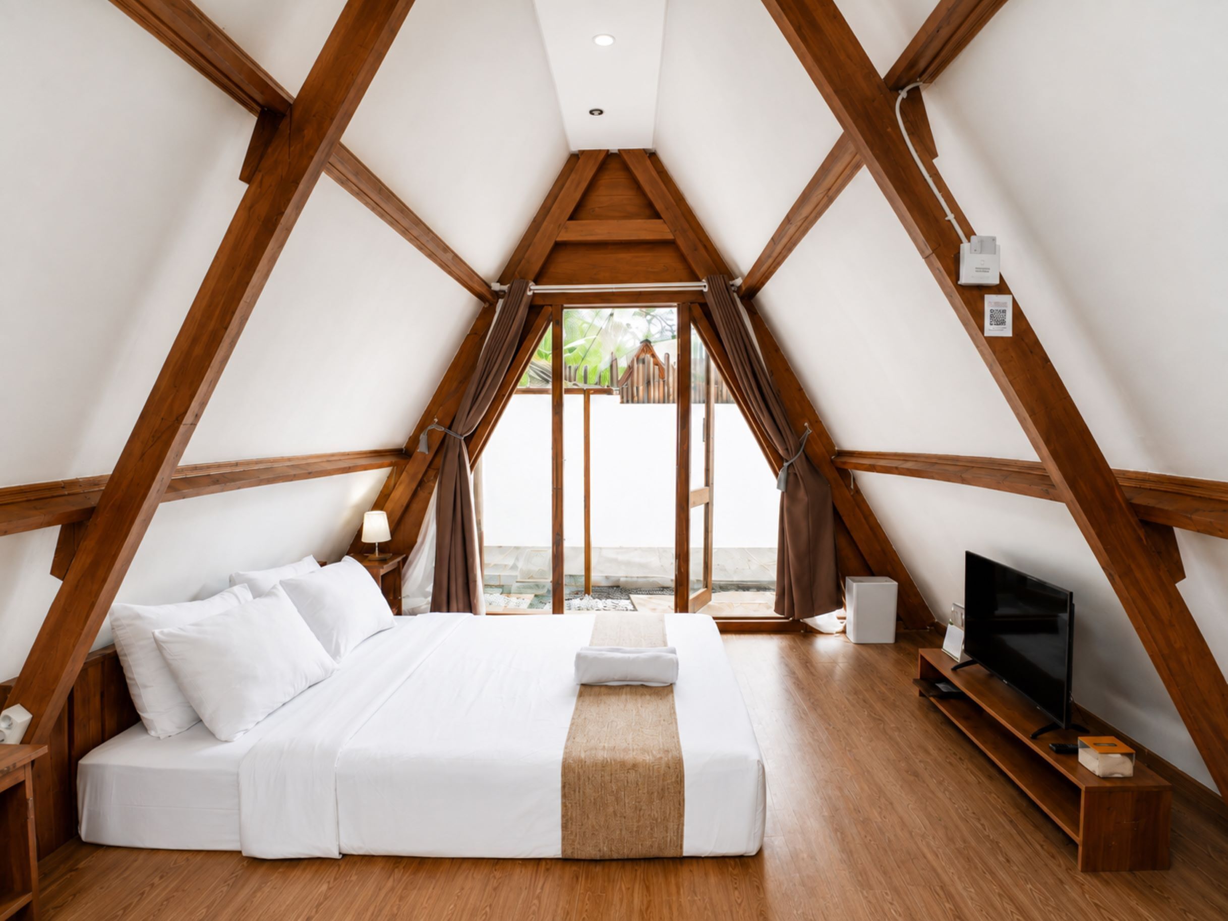 Une chambre avec un grand lit, des poutres en bois, une télévision et une fenêtre.