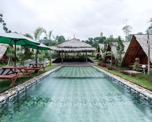 A swimming pool with wooden benches and thatched-roof structures. - New Dgyp Resort Ciater (Ciater)