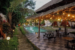 A poolside area with checkered flooring, wooden furniture, and string lights.