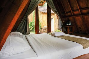 A bedroom with a large bed, a wooden table, and a view of a wooden structure outside.