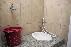 Une salle de bain avec une douche, des toilettes et un seau rouge.