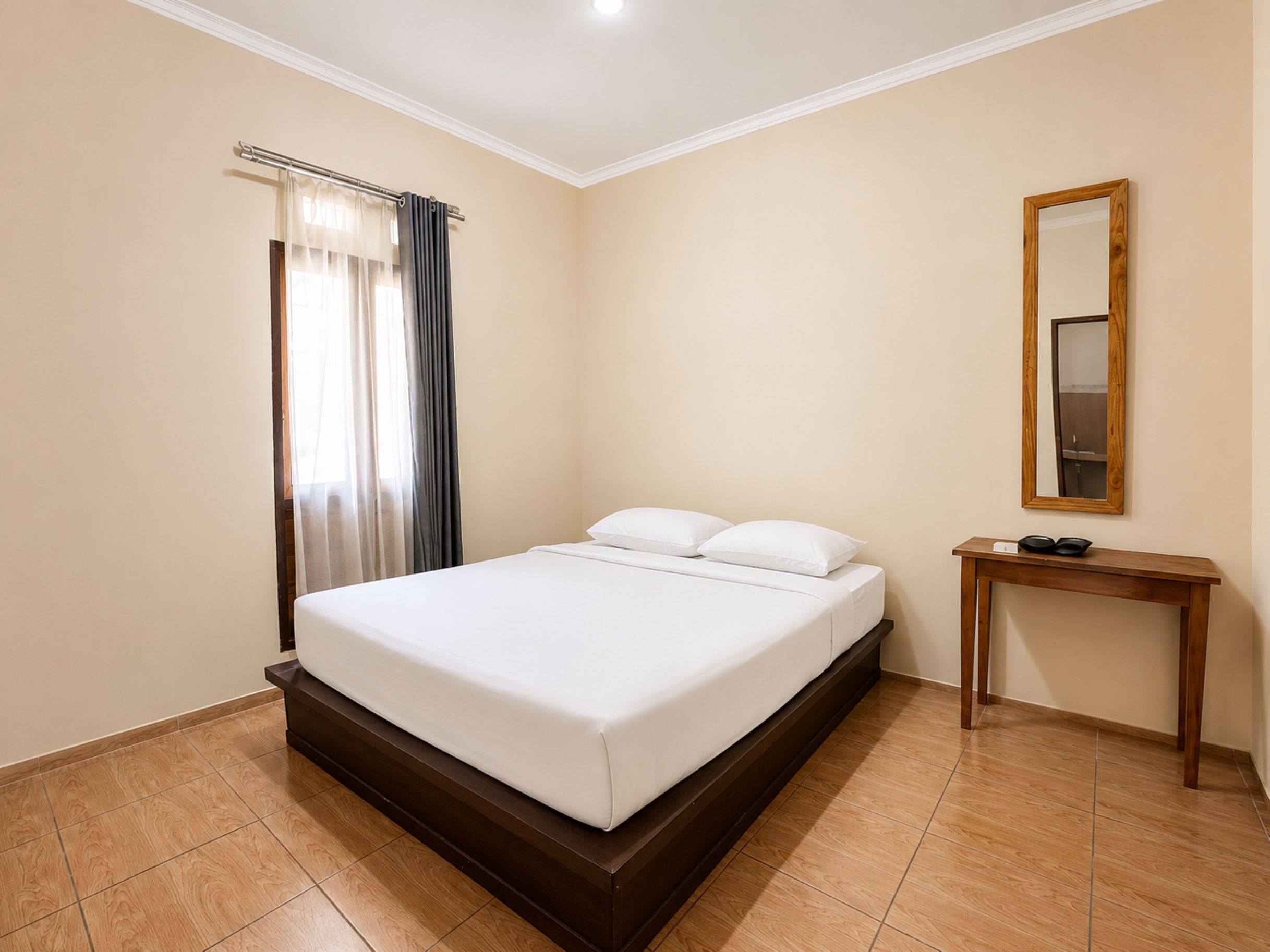 Een hotelkamer met een bed, nachtkastje, spiegel en raam met gordijnen.