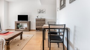 Un salon moderne avec une table à manger en bois, des chaises noires, un téléviseur posé sur un meuble en bois et des œuvres d’art décoratives accrochées au mur.