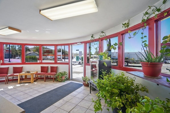 A hotel lobby with red-framed windows, a reception desk, seating area, and potted plants.