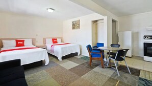 Une chambre d’hôtel avec deux lits, une table à manger avec des chaises, un coin cuisine et une porte donnant sur une autre pièce.