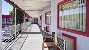 A covered corridor with a metal railing, a wooden chair, and a window with a number sign.