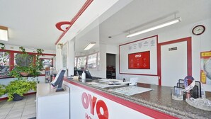 A reception desk with a red and white color scheme, a clock on the wall, and a sign indicating the hotel name.
