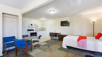 Une chambre de taille modeste comprenant un lit, un bureau, une chaise, une petite kitchenette et un téléviseur.