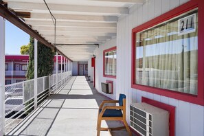 A covered balcony with a metal railing, a wooden chair, and a window with a curtain. - King Bed | Non-Smoking (Alpine TX)
