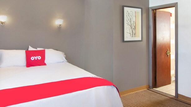 A hotel room with a bed, a red OYO pillow, a framed picture on the wall, and a door leading to another room. - Full Bed|Wilkes-Barre PA (Wilkes-Barre PA)
