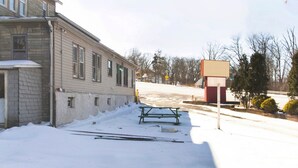 Rua coberta de neve com um edifício, uma mesa de piquenique e uma quadra de basquete.