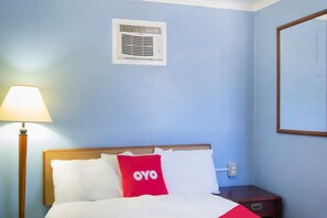Una habitación de hotel con cama, mesita de noche, lámpara y aire acondicionado instalado en la pared.