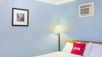 A hotel room with a bed, a lamp, a framed picture on the wall, and a wall-mounted air conditioner.