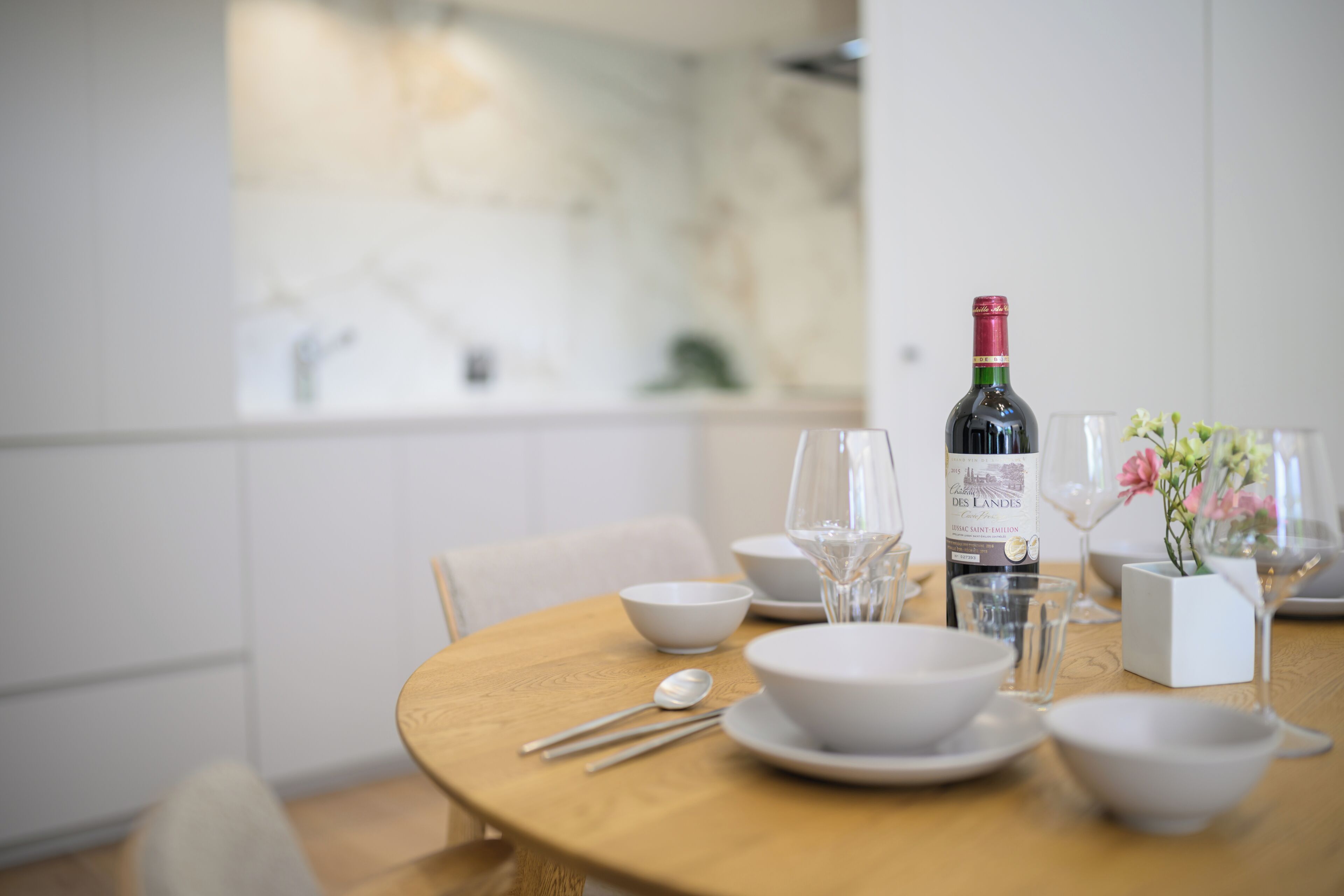 A dining table set with white bowls, wine glasses, and a bottle of wine.