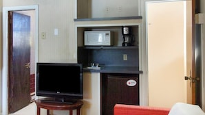 Habitación compacta con televisión, microondas, cafetera y un mueble pequeño.