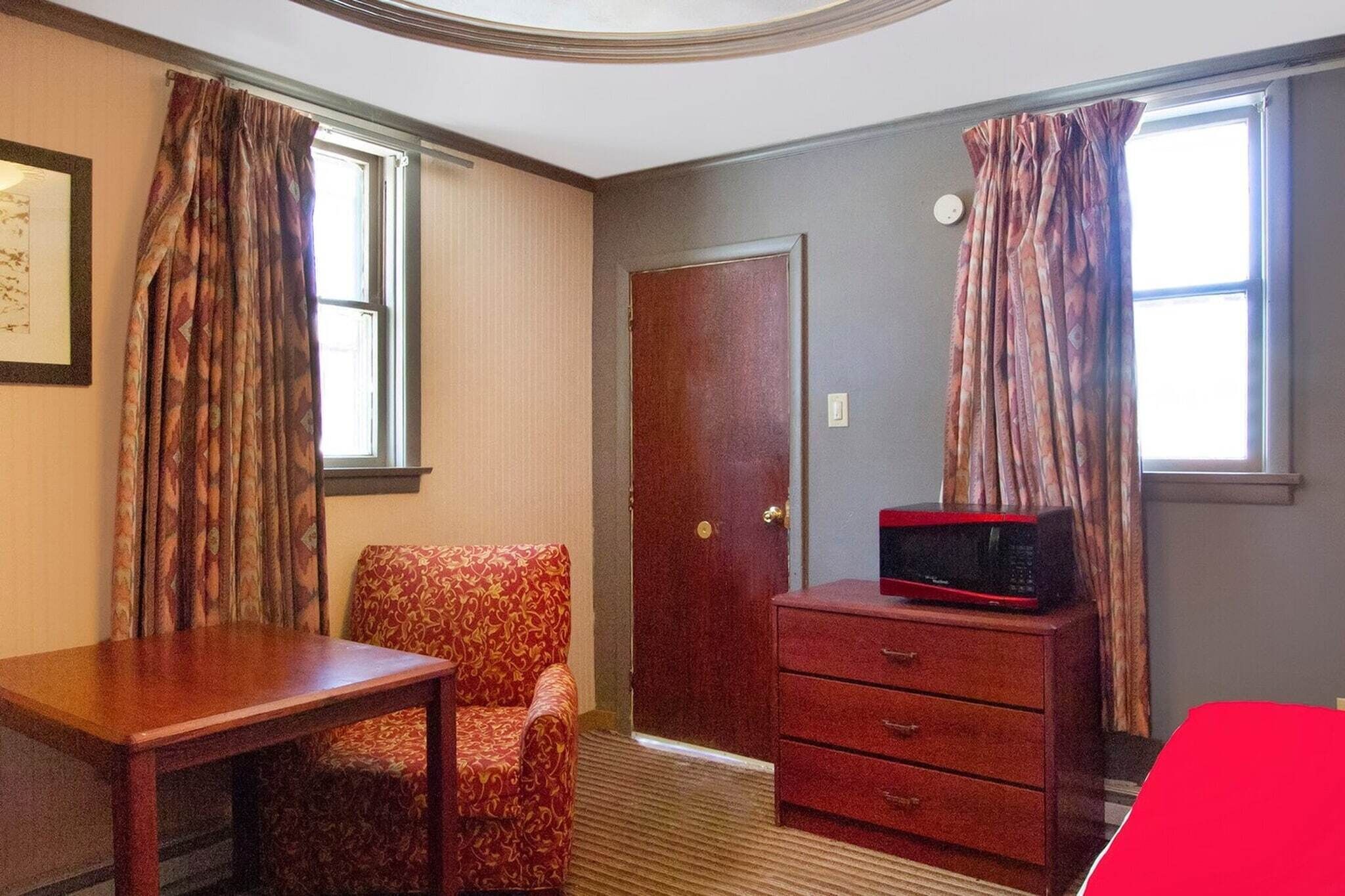 A room with a wooden desk, a patterned armchair, a dresser with a microwave, and a door.