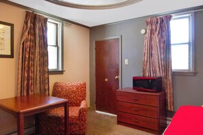 A room with a wooden desk, a patterned armchair, a dresser with a microwave, and a door.