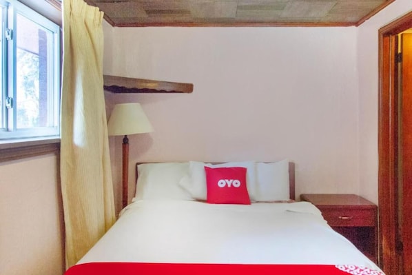 A hotel room with a bed, a bedside table, a lamp, and a window with curtains.