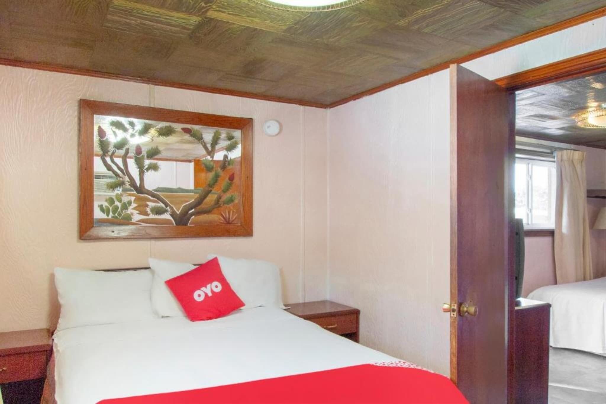 Habitación de hotel con cama, mesita de noche, un cuadro en la pared y una puerta que da a otra habitación.