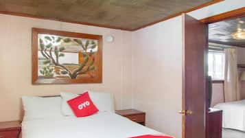 Habitación de hotel con cama, mesita de noche, un cuadro en la pared y una puerta que da a otra habitación.