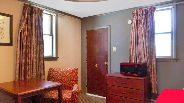 A room with a wooden desk, a patterned armchair, a dresser with a microwave, and a door. - 2 Queen Bed|Non-Smoking (Wilkes-Barre PA)