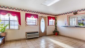 Una habitación con piso de baldosas, una puerta y ventanas con cortinas rojas.