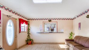 Una habitación con sofá de cuero marrón, piso de baldosas, puerta con espejo decorativo y una planta pequeña.