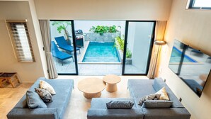 A modern living room with a grey sofa set, a coffee table, and a view of a swimming pool through glass doors.