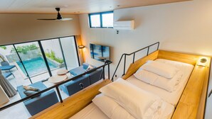 A modern hotel room with a balcony, a bed, a desk, and a view of a swimming pool.