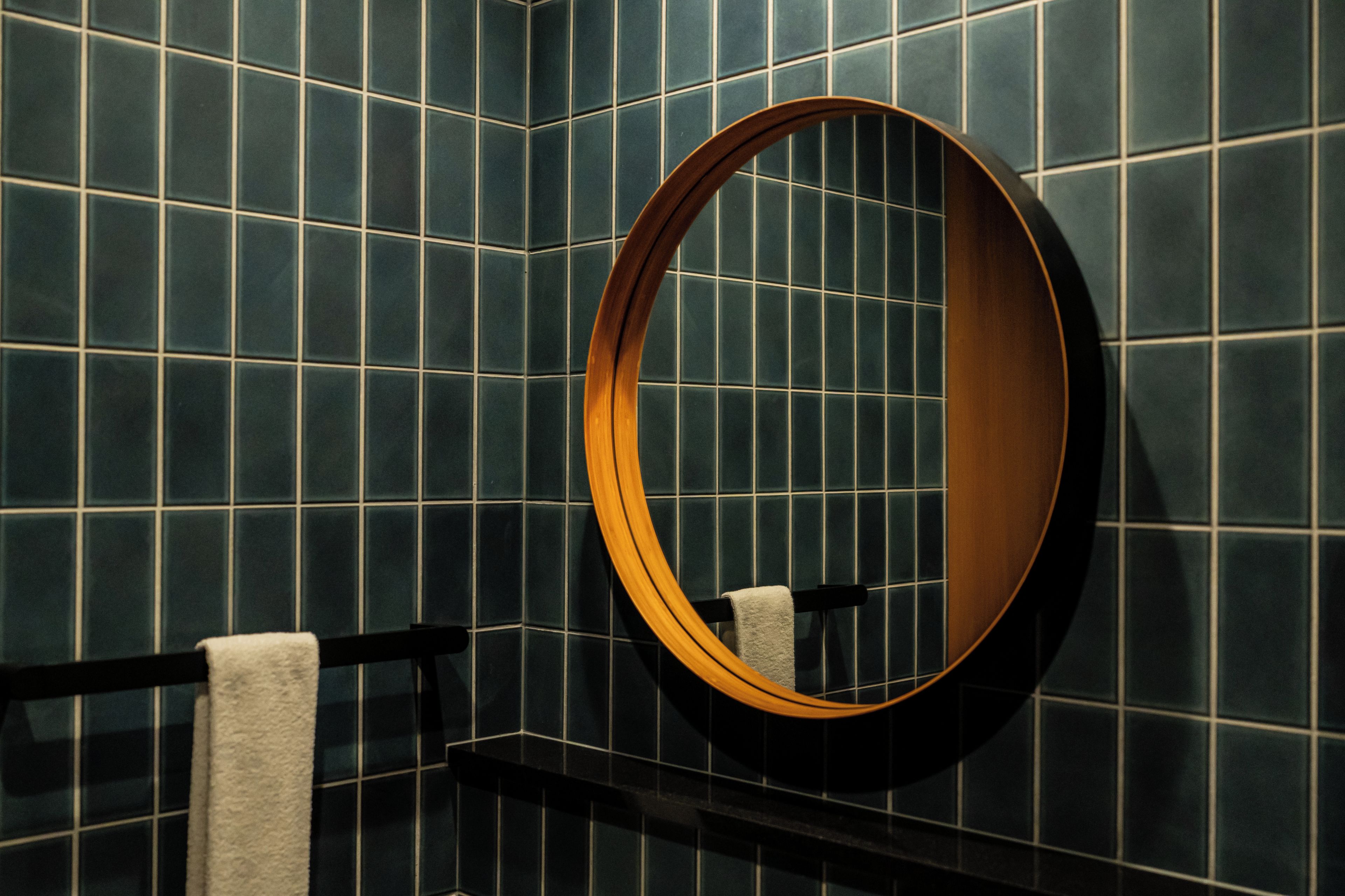 A bathroom with dark blue tiles, a wooden-framed mirror, and a towel rack with a white towel.