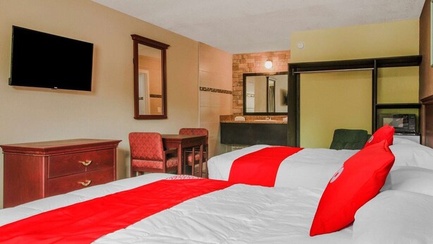 Una habitación de hotel con cama, televisor, escritorio, silla y espejo.