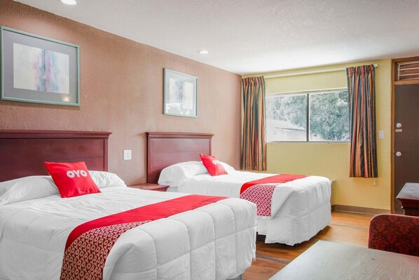 A hotel room with two beds, a wooden headboard, a window with curtains, and a door.