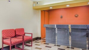 Un área de recepción con mostrador, dos sillones rojos estampados y un mostrador de registro.