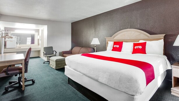 A hotel room with a large bed, a desk, a chair, a small table, and a lamp. - Bald Knob AR|King Bed|Smoking (Bald Knob AR)