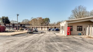 A parking lot with several cars, a building with a red door, and a row of apartment buildings in the background. - Bald Knob AR|King Bed|Smoking (Bald Knob AR)