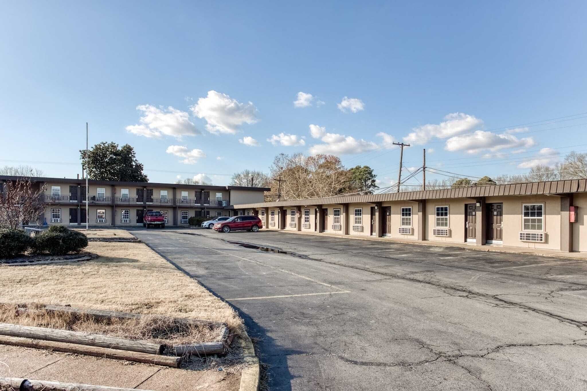 Un motel con un parcheggio, un edificio con diverse finestre e cielo sereno.