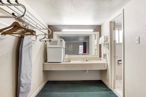 Un baño pequeño con microondas, perchero y cortina de ducha.