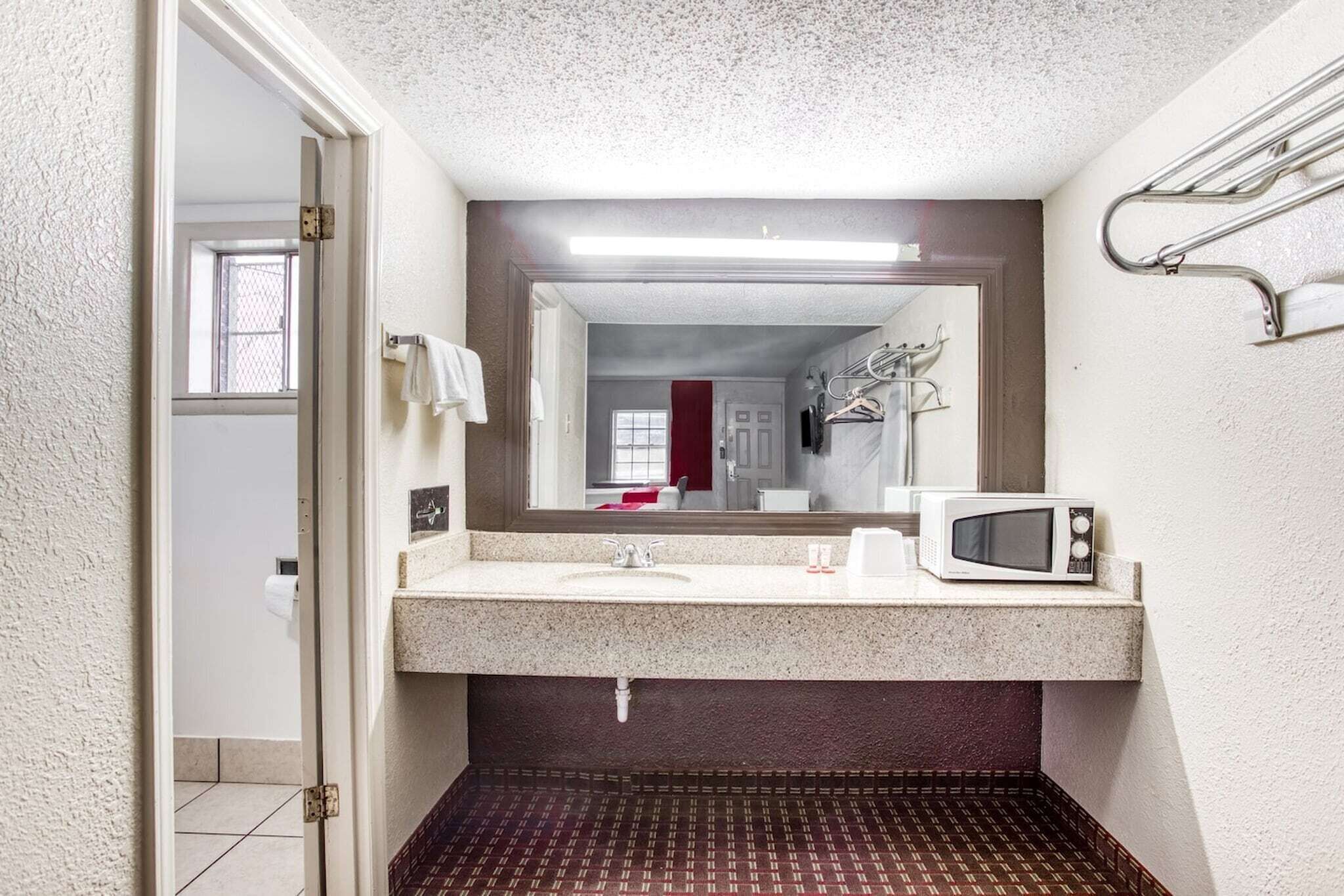 Een badkamer met een wastafel, spiegel, handdoekhouder en een magnetron.
