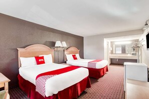 Ein Hotelzimmer mit zwei Betten, jeweils mit einer rot-weißen Bettdecke, einem Holz-Kopfteil, Nachttischlampen und einem kleinen Tisch.