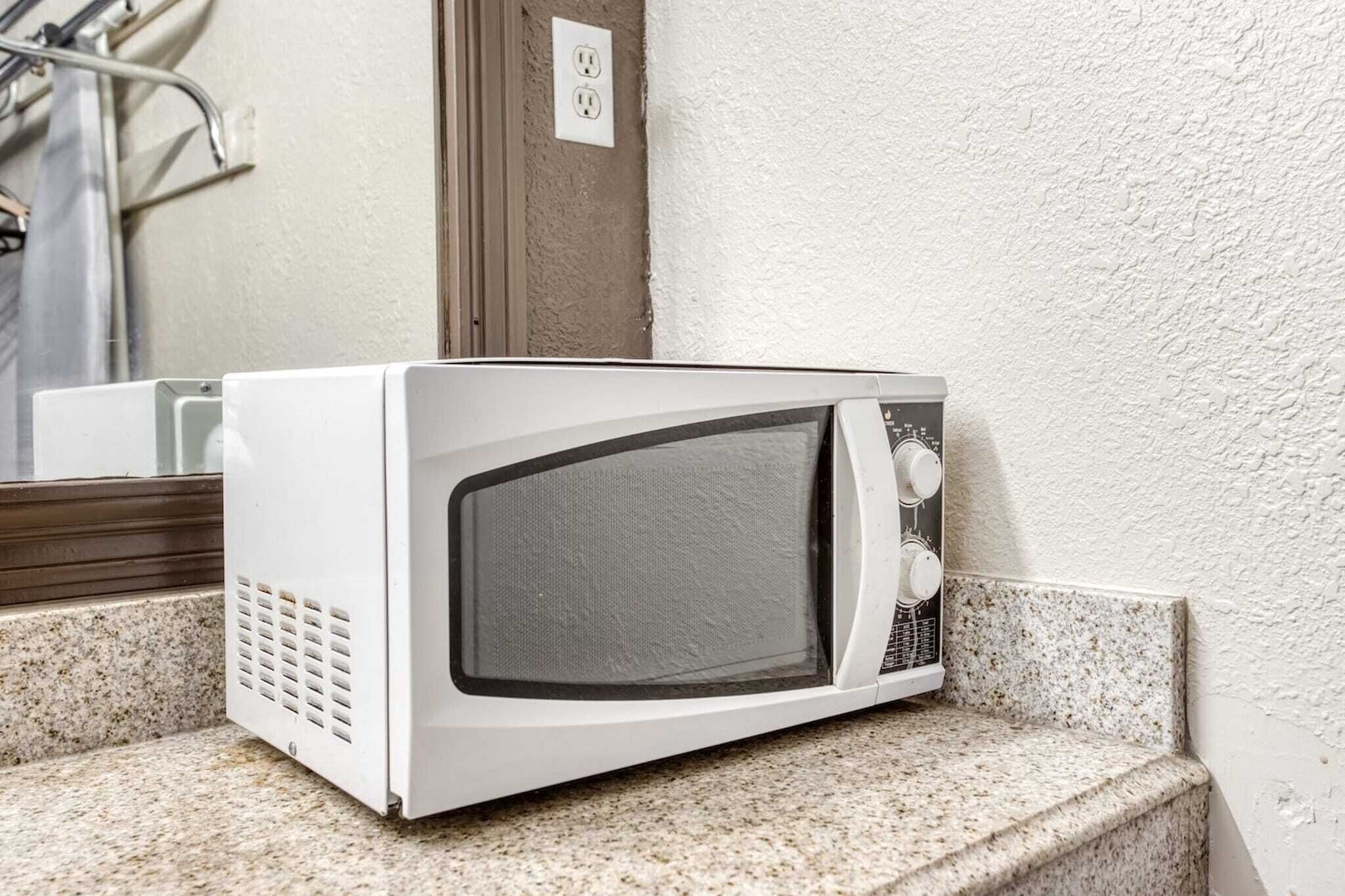 A white microwave on a granite countertop near a white textured wall.