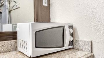 A white microwave on a granite countertop near a white textured wall.