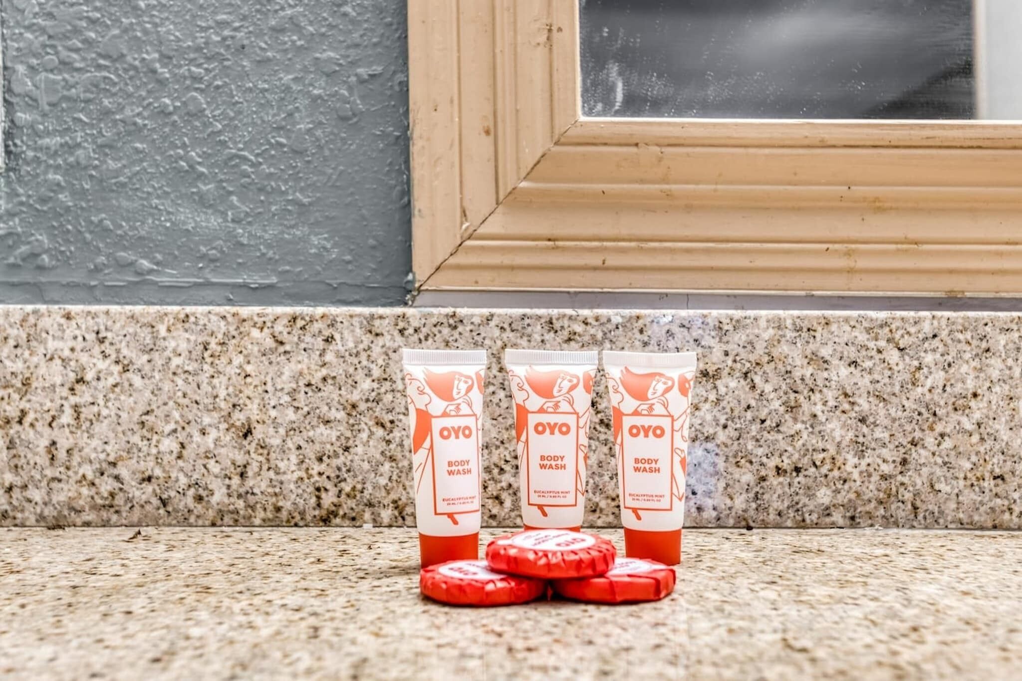 Three OYO body wash bottles and four red circular objects on a granite countertop.