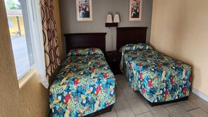A room with two beds, a window with curtains, two wall-mounted lamps, and two framed pictures.