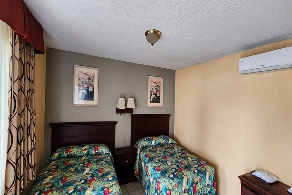 Une chambre d’hôtel avec deux lits, un luminaire au plafond, deux lampes fixées au mur et un appareil de climatisation.