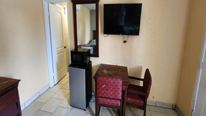 A small room with a kitchenette, a television mounted on the wall, a door leading to another room, and a table with two chairs.