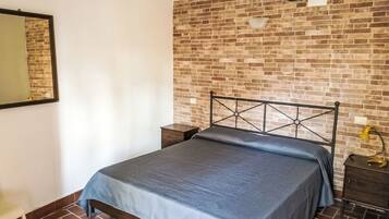 Ein Schlafzimmer mit einer Ziegelwand, einem Bett mit Metallgestell, einem Nachttisch, einer Lampe und einem Spiegel an der Wand.