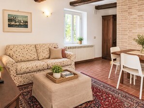 Ein Wohnzimmer mit einer Couch, einem Hocker und einem Essbereich mit Stühlen und einem Tisch.