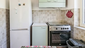 Eine kleine Küche mit einem weißen Kühlschrank, einem kleinen weißen Backofen und einem hellgrünen Schrank darüber.