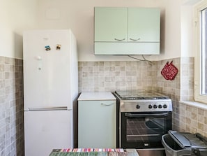 Eine kleine Küche mit einem weißen Kühlschrank, einem kleinen weißen Backofen und einem hellgrünen Schrank darüber.